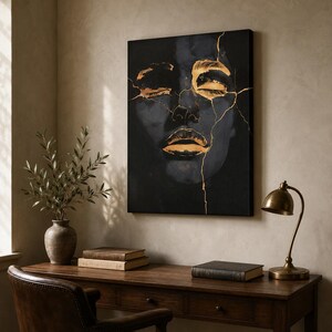 May include: A rectangular wall art canvas featuring a dark, shadowy face with closed eyes and lips highlighted in metallic gold. Thin, jagged gold lines resembling cracks run across the face, contrasting against the deep black background.