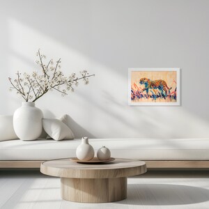May include: A framed artwork featuring a cheetah in a colorful, abstract style. The cheetah is depicted with orange spots and is set against a backdrop of tall, colorful grass. The artwork is displayed in a white frame.