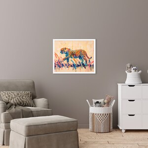 May include: A framed watercolor painting of a cheetah in a field of tall grass. The cheetah is depicted with orange spots and blue and yellow accents. The artwork is set against a beige background.