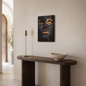 May include: A rectangular canvas wall art piece featuring a dark, moody portrait of a face with closed eyes. The image is accented with metallic gold paint strokes that trace lines across the forehead, eyes, and lips, resembling kintsugi art.