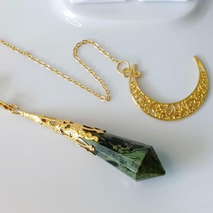 May include: A gold chain with a green crystal pendulum and a gold crescent moon charm. The pendulum is faceted and has a gold-plated metal top.