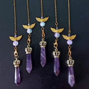 May include: Set of six amethyst crystal pendulums with gold-tone angel wings and crowns. Each pendulum features a purple amethyst crystal point, a gold-tone crown, and a pair of angel wings.