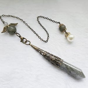 May include: A silver chain with a grey crystal pendulum, a grey crystal bead, a silver angel charm, and a white pearl bead.
