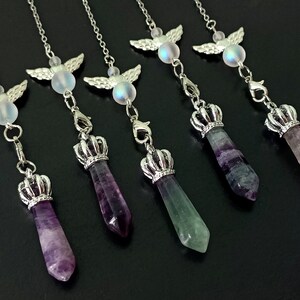 May include: Six silver and crystal pendulums with angel wings and crown charms. The pendulums are made of fluorite in shades of purple, green, and blue.