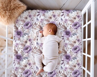 Op de afbeelding: Een baby slaapt op een wit ledikantlaken met een paars en bruin bloemenpatroon.