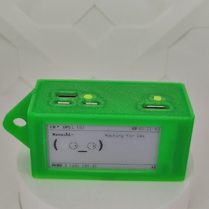 May include: A vivid green rectangular device with a small screen displaying text and a cartoon face. The device has several ports and a loop on the side. The screen shows the text "CH APS1 (8)", "Hanashi", and "Waiting for 14s".