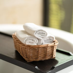 Può includere: Un cesto di vimini pieno di tre asciugamani bianchi arrotolati su una superficie nera.