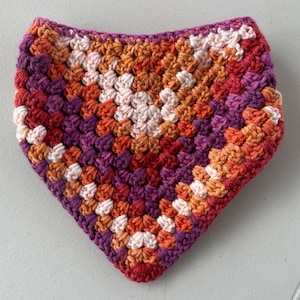 May include: A crocheted triangle scarf in shades of orange, red, purple, and white.
