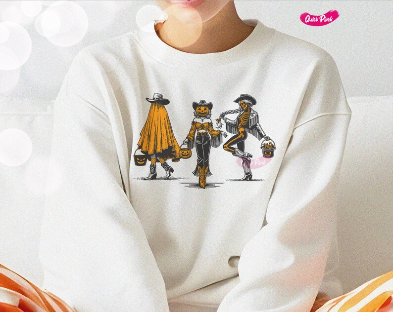 May include: White sweatshirt featuring a Halloween-themed graphic. The design depicts three figures: a ghost, a pumpkin-headed cowgirl, and a skeleton, each holding a trick-or-treat bucket. The figures are in a line, walking forward.