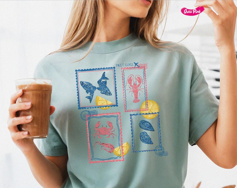Pode incluir: Uma camiseta azul clara com quatro desenhos de selos postais representando frutos do mar. Os selos mostram peixes, uma lagosta, um caranguejo e ostras, com fatias de lim&atilde;o. O texto "FIRST CLASS" &eacute; impresso acima dos selos.