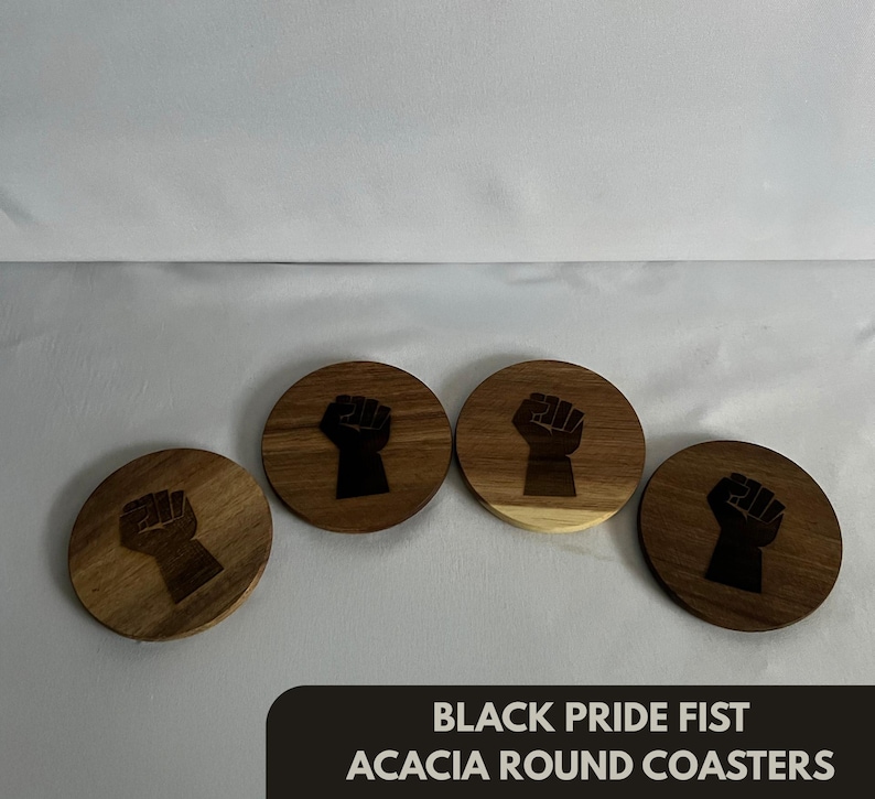 May include: Four round acacia wood coasters with a black fist design. The coasters are arranged on a light surface. The text "BLACK PRIDE FIST ACACIA ROUND COASTERS" is at the bottom.