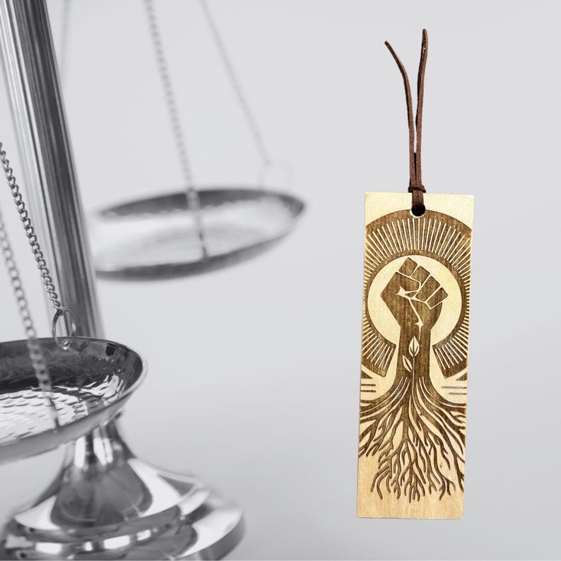 Wooden Black Pride bookmark with a leatherette tassel resting inside an open book, styled in a cozy reading setting. A perfect gift for book lovers, scholars, and those who cherish cultural heritage.