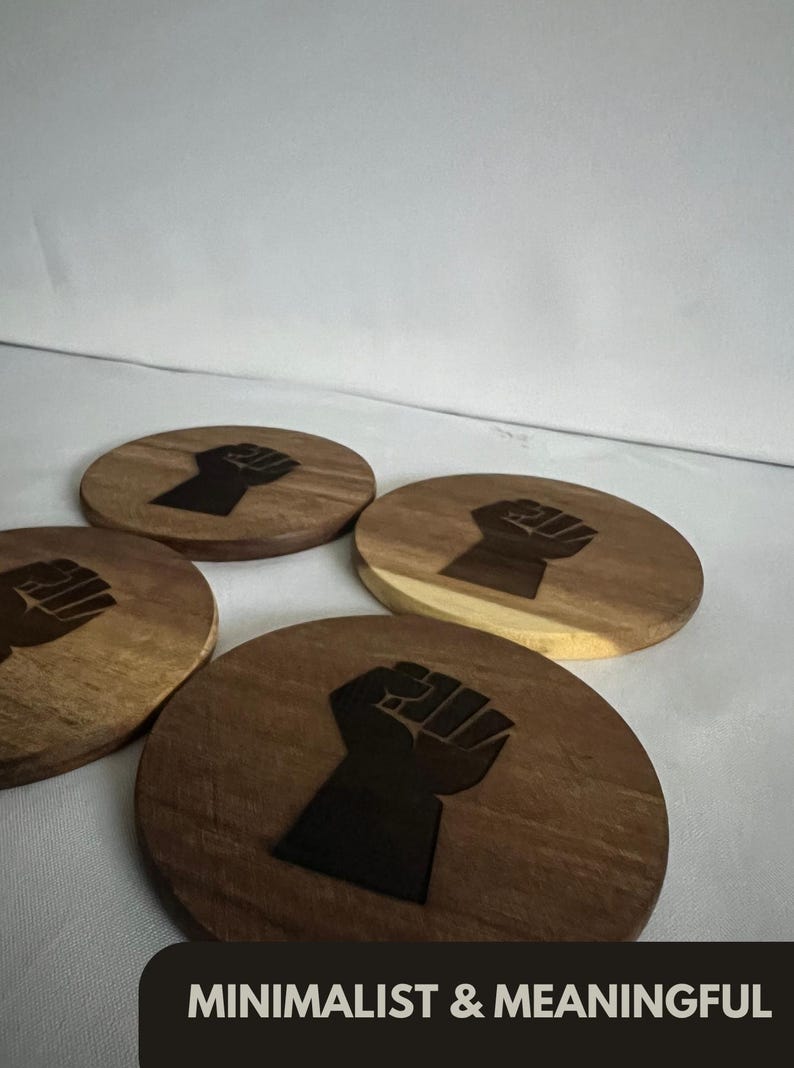 May include: Four wooden coasters with a dark brown finish and a black fist graphic. The coasters are round and feature a minimalist design. The text "MINIMALIST & MEANINGFUL" is at the bottom.