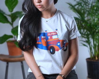 May include: White t-shirt featuring a colorful graphic of a bus with the word "PILIPINAS" on it. The shirt has rolled-up sleeves and is being worn by a person.