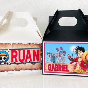 May include: Two One Piece themed party favor boxes. One box is white with a skull and crossbones logo and the name "RUAN". The other box is black with a One Piece character and the name "GABRIEL".