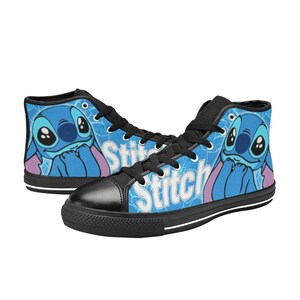 May include: A pair of black high-top canvas shoes with a blue and white print featuring Stitch from Lilo & Stitch. The print includes the word "Stitch" in white letters.
