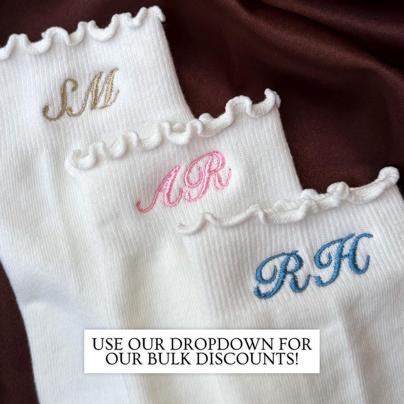 Embroidered initial socks with feminine ruffle edges styled on dark brown satin showcasing luxury inspired personalized pilates socks with elegant monogram embroidery ideal for barre class outfits yoga lovers bridesmaid gifts birthday gifts for women bachelorette weekend welcome bags and matching girls trip accessories featuring soft ribbed white socks with trendy clean aesthetic embroidery that creates a chic boutique style gift for everyday wear lounging and fitness fashion