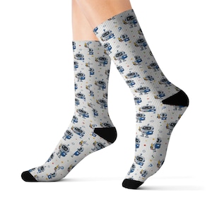 May include: Crew socks featuring a repeating pattern of small blue and grey robots on a white background with thin vertical grey stripes. The socks have solid black heels and toes, and the robot design includes small yellow and red star accents.