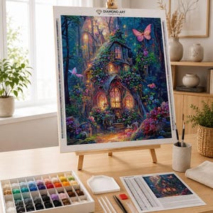 May include: A diamond art kit featuring a canvas on a wooden easel displaying a fantasy cottage in a forest with butterflies, flowers, and glowing windows. Includes a white tray, a multi-compartment storage box with colorful beads, and tools.