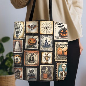 May include: Black tote bag featuring a collage of vintage Halloween-themed postage stamp designs. The stamps depict classic spooky imagery like bats, pumpkins, ghosts, and skeletons. The bag has black handles and is held by a person.