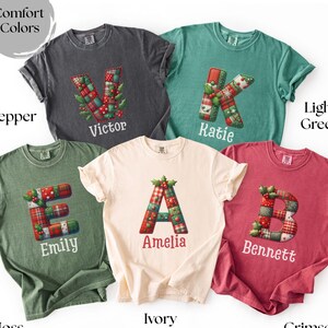 May include: Comfort Colors t-shirts in various shades, each displaying a large letter design with a patchwork pattern and a name beneath. Colours include pepper, light green, moss, ivory, and crimson. The letters are decorated with holly.