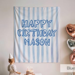 May include: A rectangular fabric wall hanging featuring vertical light blue and white stripes with the text HAPPY BIRTHDAY MASON printed in a bold blue font. The banner is displayed behind a small birthday cake and a child in a party hat.