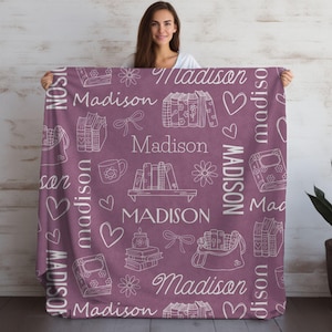 May include: A pink fleece blanket with a white repeating pattern of books, hearts, flowers, and the name "Madison".