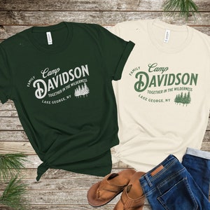 May include: Two t-shirts with a vintage camp logo design. The green shirt says "Camp Davidson Family Together in the Wilderness Lake George, NY". The beige shirt says "Camp Davidson Family Together in the Wilderness Lake George, NY".