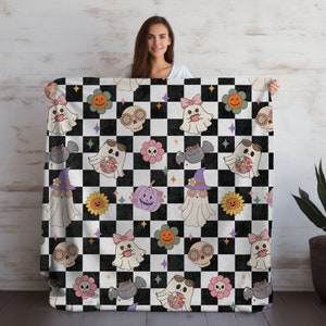 May include: A black and white checkered throw blanket with a Halloween theme. The blanket features a repeating pattern of ghosts, pumpkins, flowers, and skulls in various colors.