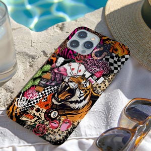 May include: A colorful phone case with a collage design featuring a roaring tiger, playing cards, roses, and a skull. The case has a mix of patterns, including leopard print, zebra stripes, and a checkered flag. Sunglasses and a straw hat are nearby.