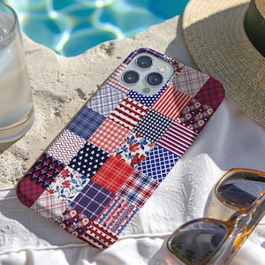 May include: A patchwork phone case in red, white, and blue, featuring various patterns like stars, stripes, and floral designs. The case is next to a straw hat, sunglasses, and a glass of water, suggesting a summer theme.