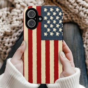 May include: A phone case featuring the American flag design. The case has a blue upper-left corner with white stars and red and cream-colored stripes. The phone case has a dual-lens camera.