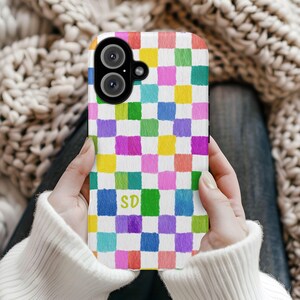 May include: A colorful phone case featuring a checkerboard pattern in shades of pink, yellow, green, blue, and purple. The case has a white background and the initials "SD" in green. The phone case has a dual-lens camera.