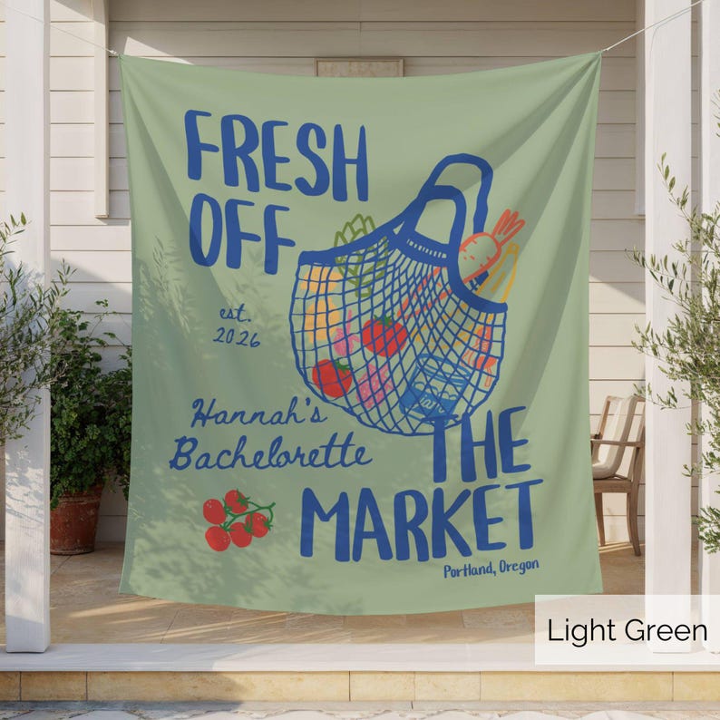 Peut inclure: Une banni&egrave;re en tissu vert clair avec un graphique bleu repr&eacute;sentant un sac de march&eacute; en filet rempli de l&eacute;gumes. Le texte indique FRESH OFF THE MARKET, est. 2026, Hannah's Bachelorette, et Portland, Oregon, avec des tomates rouges dessin&eacute;es.