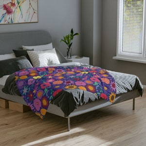 May include: A bed with a floral patterned duvet cover. The duvet cover features a variety of colorful flowers, including pink, yellow, orange, and red. The bed is made with a dark gray comforter and pillows.