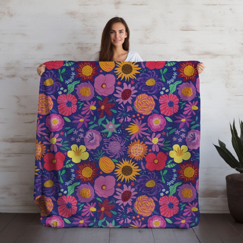 A woman holding a large fleece blanket with a bold wildflower pattern with bright pinks, purples, orange, and blues.