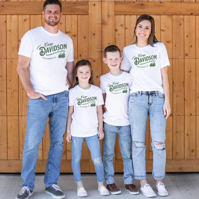 May include: A family of four wearing white t-shirts with a green and white logo that says "Camp Davidson Together in the Wilderness Lake George, NY 1978". The family is standing in front of a wooden door.