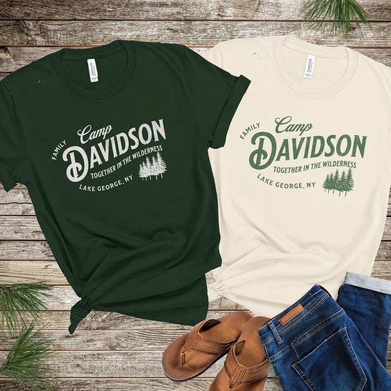 May include: Two t-shirts with a vintage camp logo design. The green shirt says "Camp Davidson Family Together in the Wilderness Lake George, NY". The beige shirt says "Camp Davidson Family Together in the Wilderness Lake George, NY".