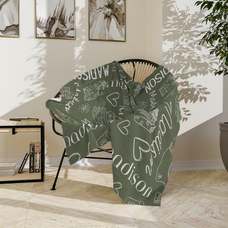 May include: A green throw blanket with a white design featuring the name "Madison" repeated throughout. The blanket is draped over a wicker chair.