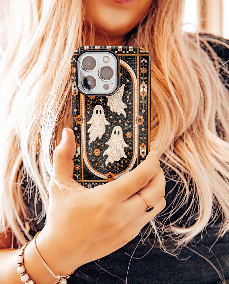 May include: A rectangular smartphone case featuring a black mosaic tile background with an arched border. The design includes three white ghost figures and small orange floral accents arranged within the central arch, creating a detailed pattern.