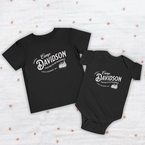 May include: Two black t-shirts with a white graphic design. The larger shirt says "Camp Davidson Family Together in the Wilderness Lake George, NY". The smaller shirt says "Camp Davidson Family Together in the Wilderness Lake George, NY".