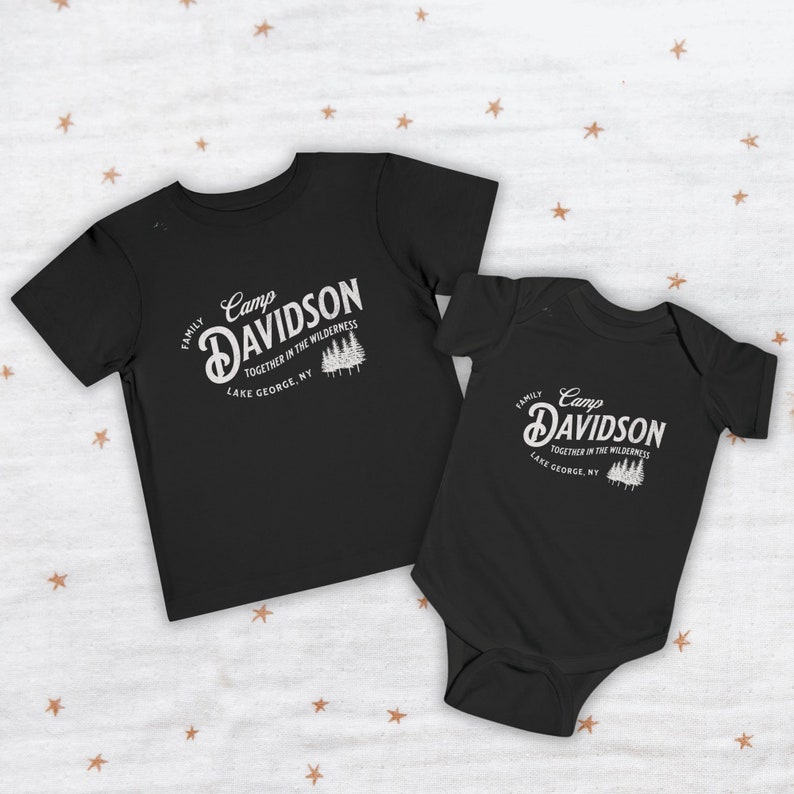 May include: Two black t-shirts with a white graphic design. The larger shirt says "Camp Davidson Family Together in the Wilderness Lake George, NY". The smaller shirt says "Camp Davidson Family Together in the Wilderness Lake George, NY".