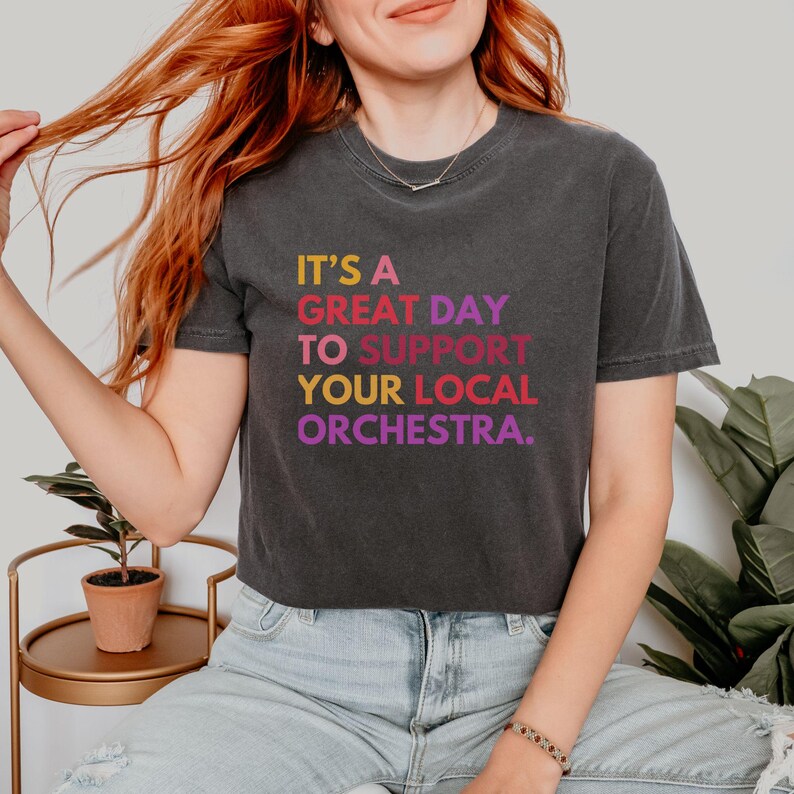 May include: A black cropped t-shirt with the text "It's a great day to support your local orchestra." in rainbow colors.