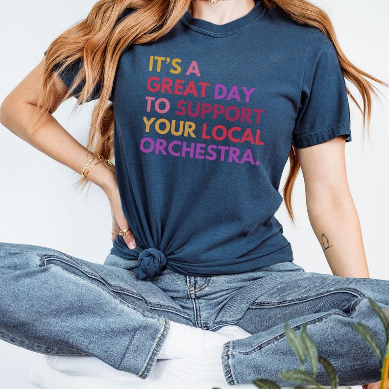 May include: A navy blue t-shirt with the text "It's a great day to support your local orchestra." in rainbow colors.
