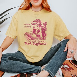 Op de afbeelding: Een geel T-shirt met een vintage illustratie van een vrouw aan de telefoon die een boek leest. De tekst op het shirt luidt "Sorry, I can't. I have a date with my Book Boyfriend."