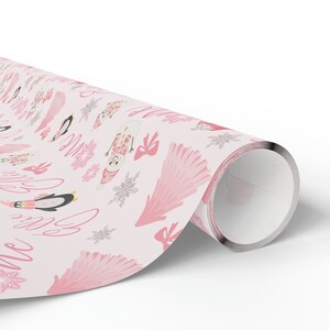 May include: Pink wrapping paper with a winter theme featuring penguins, snowmen, and snowflakes. The paper also has the words "Let it snow" written in pink cursive.