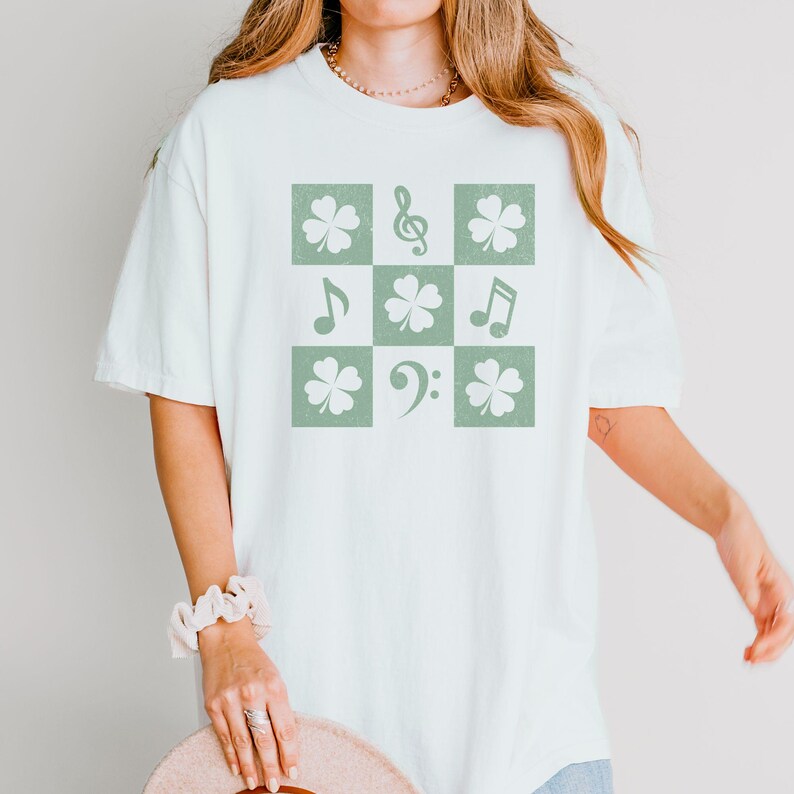 May include: A white t-shirt with a green shamrock and musical note design. The design is in a checkered pattern.