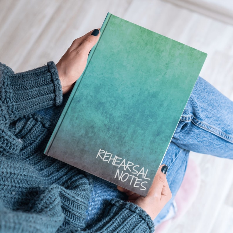 a woman holds a turquoise notebook with the words "rehearsal notes"