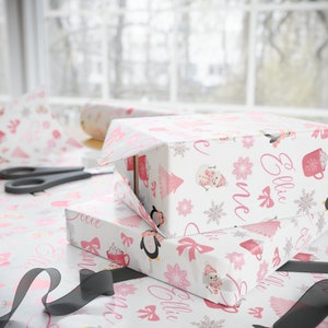 May include: Two white gift boxes with pink and white patterned wrapping paper. The wrapping paper features a snowman, penguins, snowflakes, and the name "Ellie" repeated on the paper.