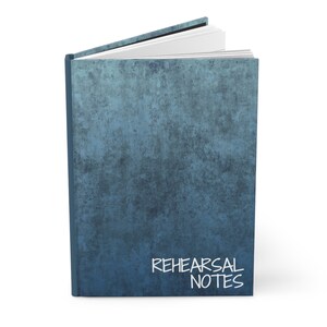 K&ouml;nnte beinhalten: Ein blaues Notizbuch mit einem abgenutzten, strukturierten Einband. Der Einband tr&auml;gt die Aufschrift "REHEARSAL NOTES" in wei&szlig;.